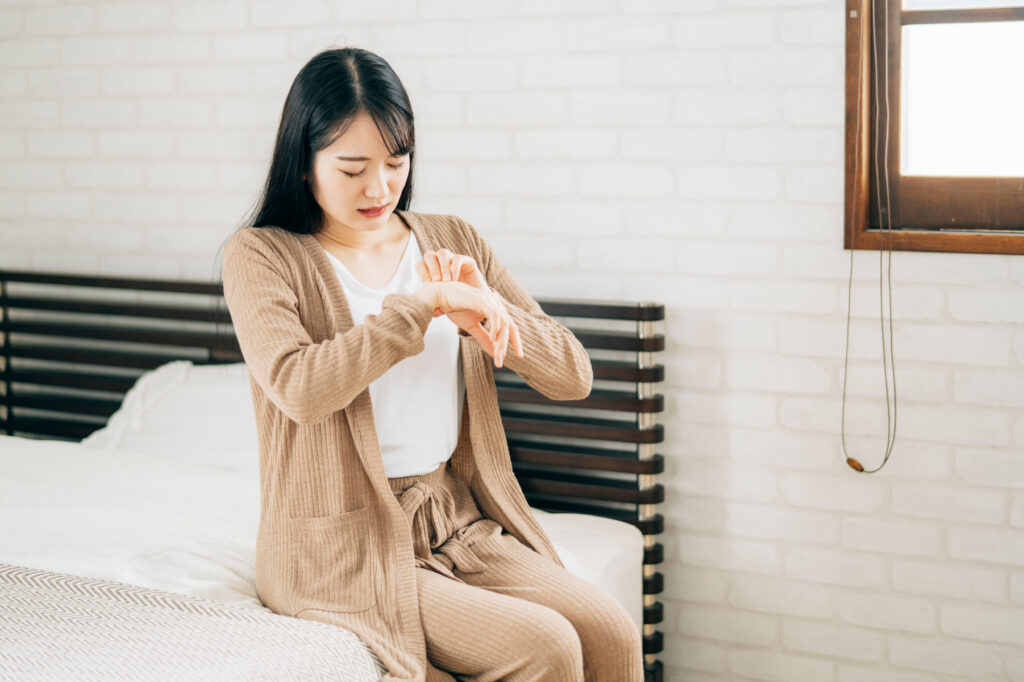 ベッドに腰かけて手をかく女性